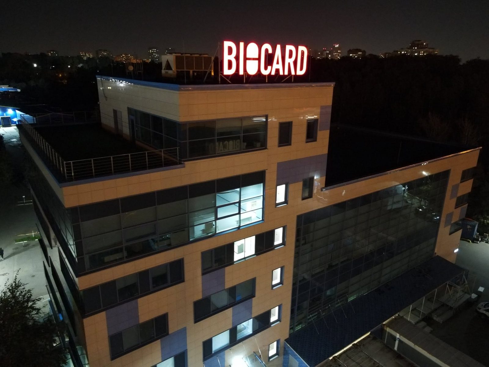 Здание BIOCARD с вечерней подсветкой, на крыше логотип компании